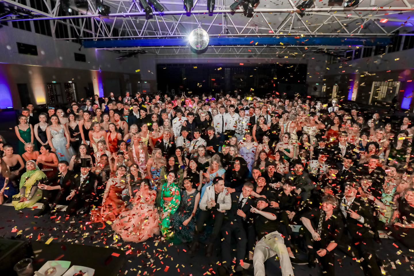 Crowd celebrating under a shower of confetti at a school formal
