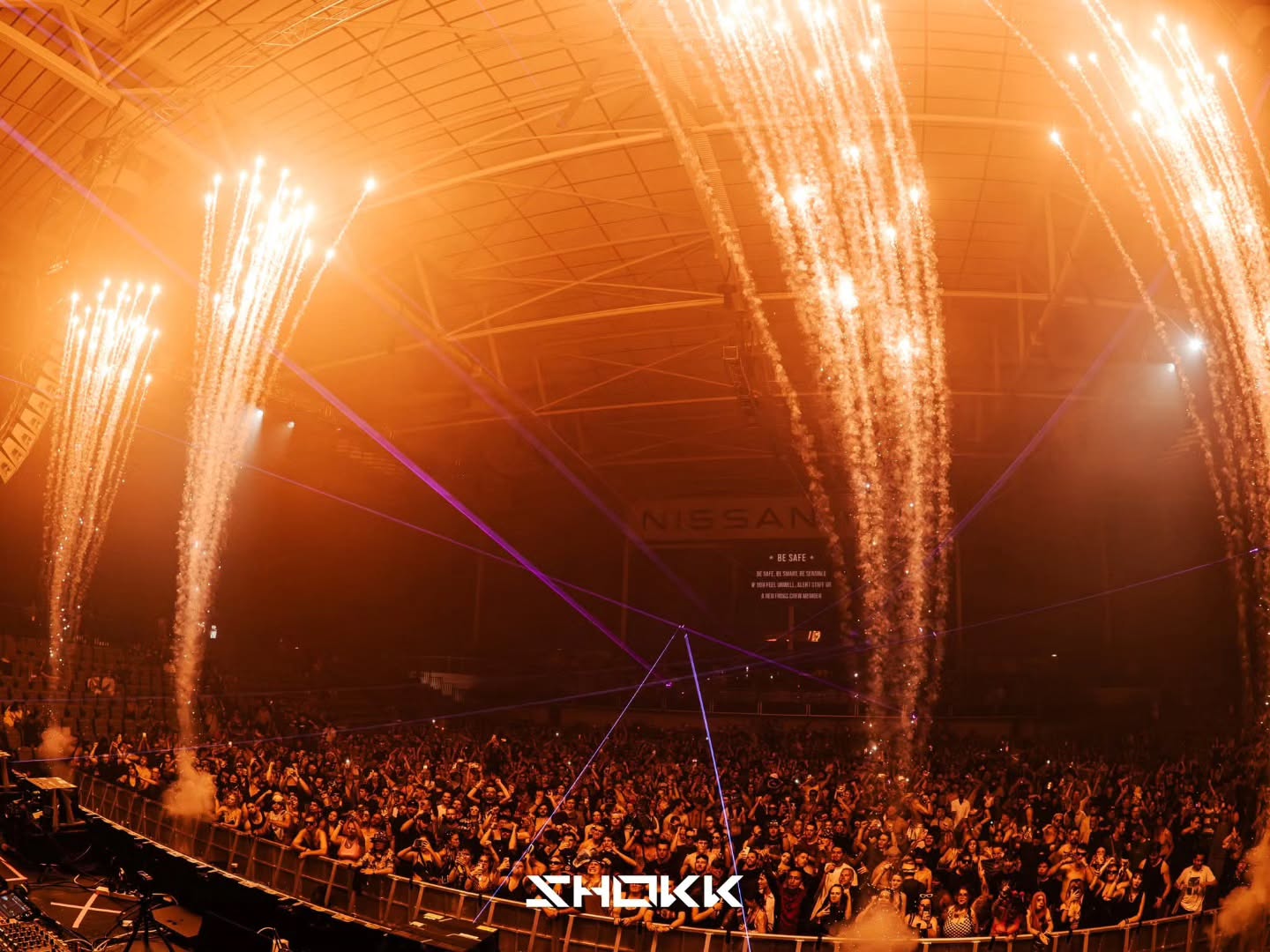 Close proximity fireworks arcing over a crowd inside an indoor arena