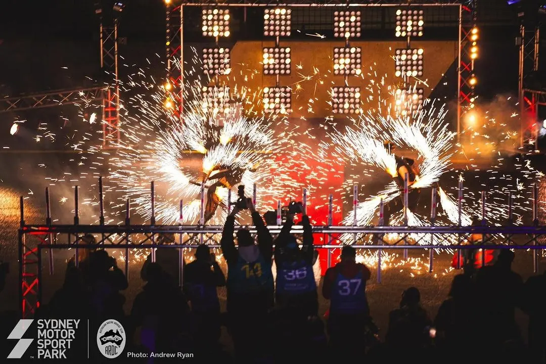 Fire performers with close proximity pyrotechnic fans watched by a crowd at Sydney Motor Sport Park