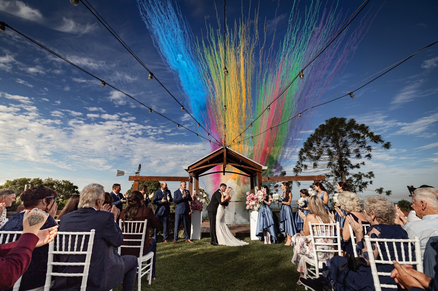 Wedding couple kissing under a rainbow of coloured smoke daytime firework effect