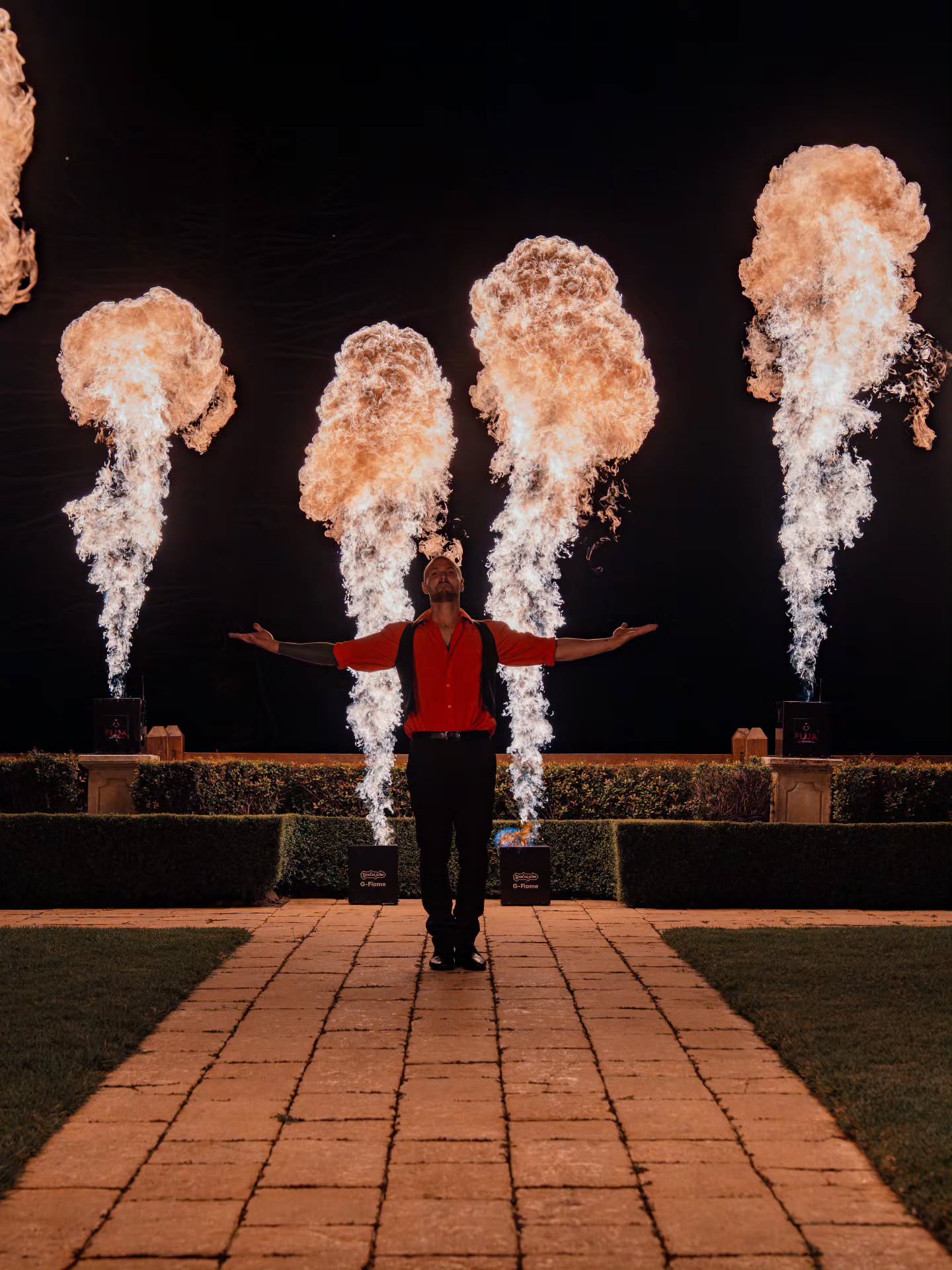 Performer with four tall flame projection bursts at a garden venue