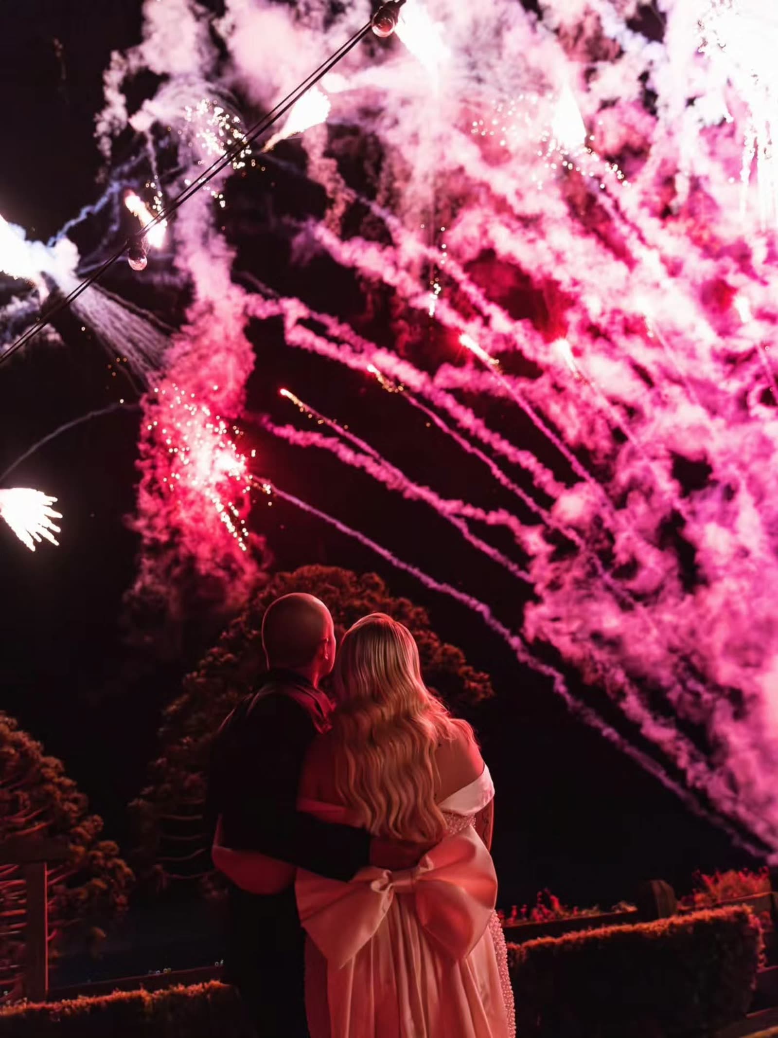 Wedding couple embracing under pink fireworks