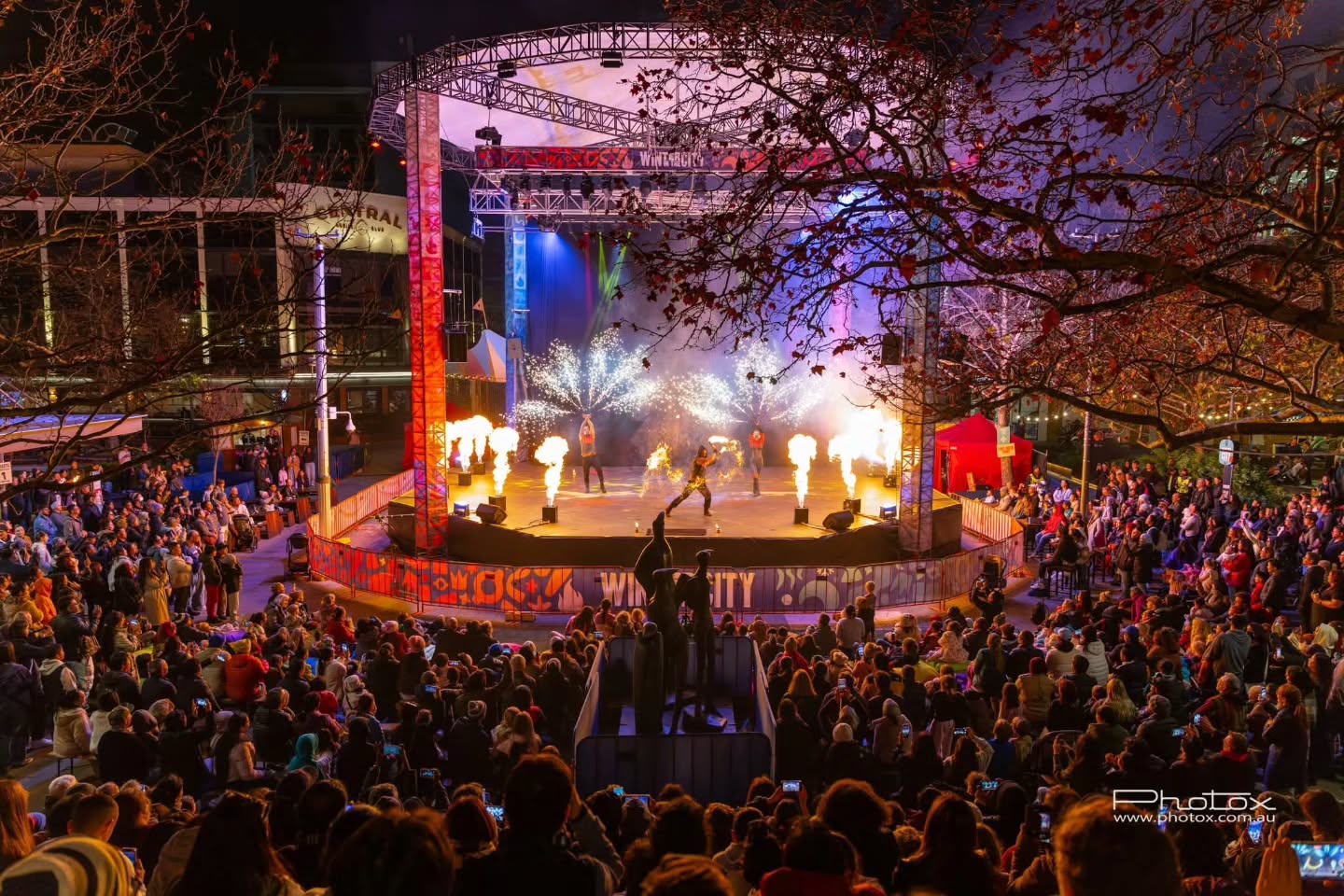 Fire performers and flame bursts on stage at a Winter City event, watched by a large crowd