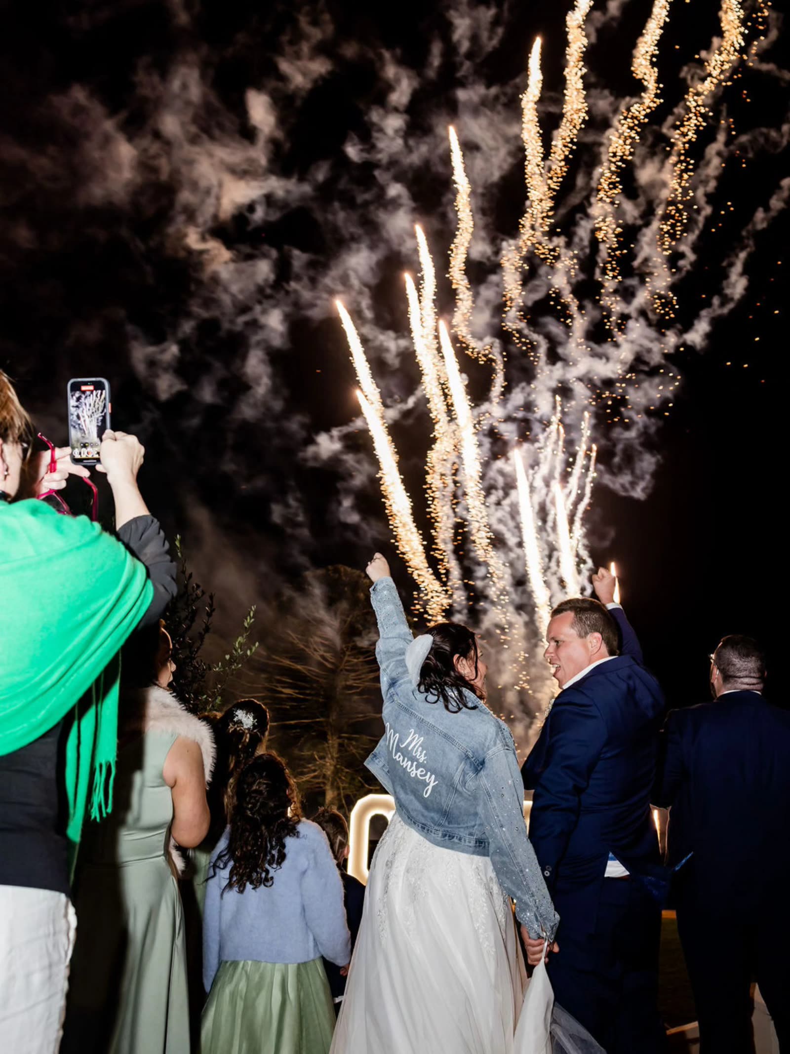 Bride and groom cheering under gold fireworks